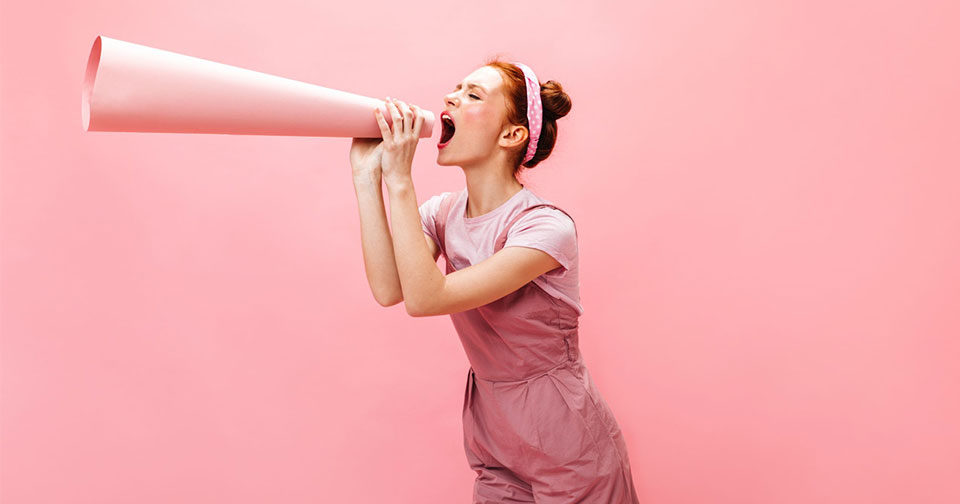 Image-mise-en-avant-article-Une-femme-énergique-crie-un-slogan-à-l'embouchure.-Portrait-de-jeune-fille-en-robe-légère-sur-fond-rose.